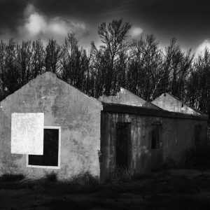 A black and a white square painted on the wall of a ruined house with dead trees and clouds in the background