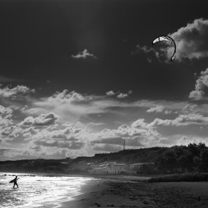 Backlit kite surfer walking toward beach with sail above him