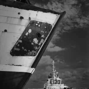 Bow of dismissed boat with moored tug in the background