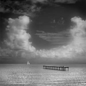 Pier and sailboat under u-shaped cloud