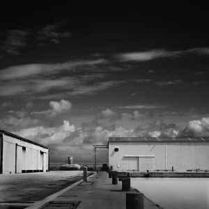 A row of bollards leading to two shipyard buildings and a man in the distance