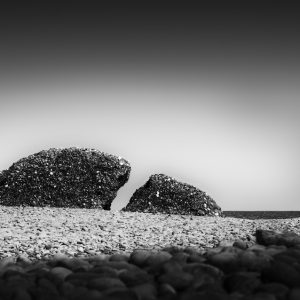 Semicircular split rock by the sea with pebbled beach in foreground