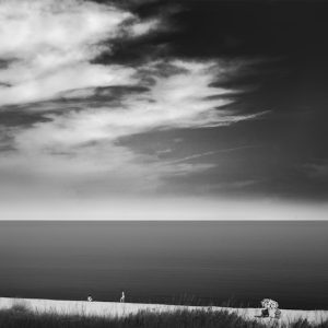 White beach with four people and two umbrellas, sea and clouds