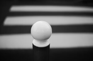 Black bollard with white ball-shaped top, zebra crossing in background