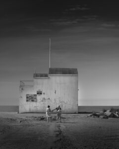 Elderly couple holding hands as they walk toward building with sea in the distance