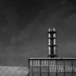 Three-tube metal chimney inside lattice tower emerging from metal structure.