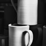 Two white unglazed mugs on top of each other with others in dark background.