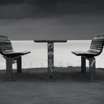 A table and two benches with sea and two promontories in background.
