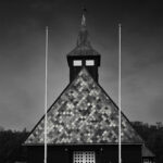 Two tall white poles in front of church with dark spire and slate roof.