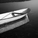White rowing boat and its reflection on water; bow and mooring line pointing at upper right corner.