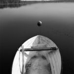 White rowing boat and mooring buoy seen from behind; trees in the distance.