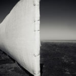 A tall white fence stretching from center to left on grassy ground with sea and clear sky ih the background.