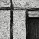 Dark wood crossing at right angles in top left and door surmounted by bricks in low right of white timber frame wall