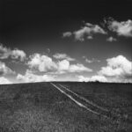 Tractor tracks diagonally crossing a grassy slope toward cloudy sky.