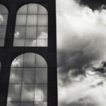 Cloud reflection in arched mirror windows of dark building, with clouds in right half of picture.