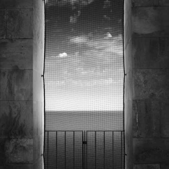 View of sea and clouds through a net that covers a window in the bell tower of the Trani Cathedral, Italy